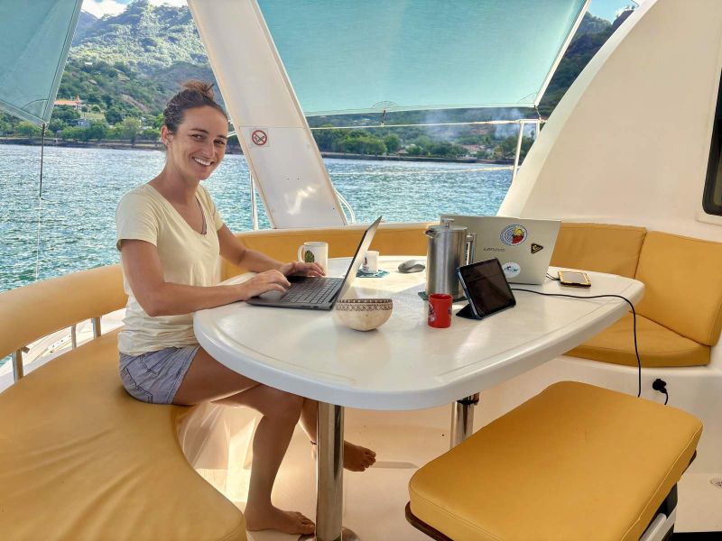 Coworking à bord : une passagère travaille sur son ordinateur dans le cockpit du catamaran, au mouillage