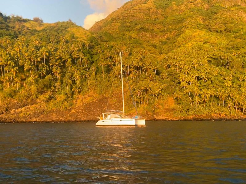 Toake Ona au mouillage dans une baie bordée de cocotiers, lumière du soir