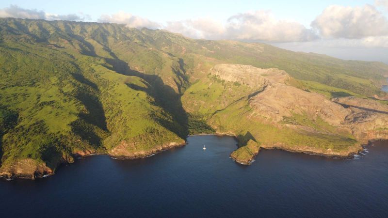 Vallée verdoyante et baie de la côte ouest de Nuku Hiva, un catamaran au mouillage